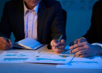 Dois homens sentados conversando. Eles estão analisando gráficos em um relatório.