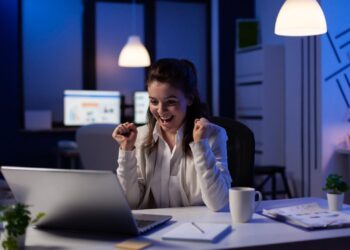 Mulher vibrando olhando para o notebook. Ela está em um escritório.