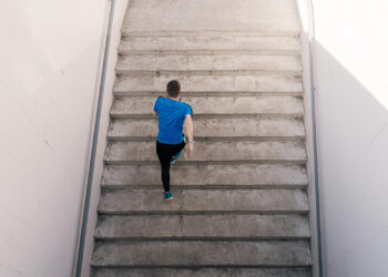 Homem de camiseta azul subindo uma escada caminhando.