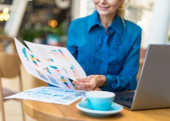 Mulher segurando alguns documentos com dados e gráficos financeiros.