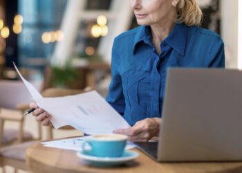 Mulher analisando alguns papéis enquanto toma um café.