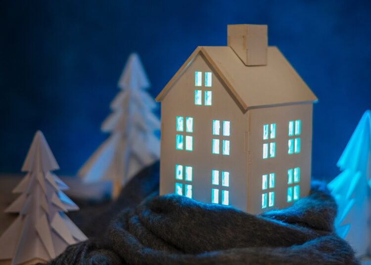Miniatura de casa rodeada de árvores. As luzes internas estão acesas em tom de azul.