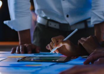 Reunião de negócios. É possível ver várias mãos manuseando relatórios e um tablet.