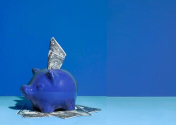 Cofrinho azul em formato de porco. Há uma cédula em cima dele.