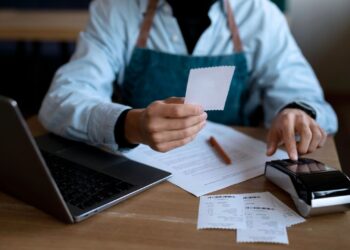 Empreendedor analisando as finanças da empresa. Ele está com um notebook e uma maquininha de cartão.