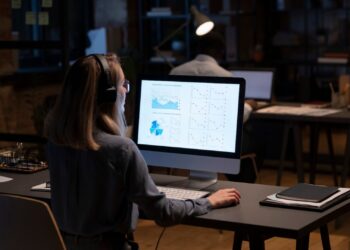 Mulher trabalhando sozinha no escritório. Ela está analisando diversos gráficos no computador.