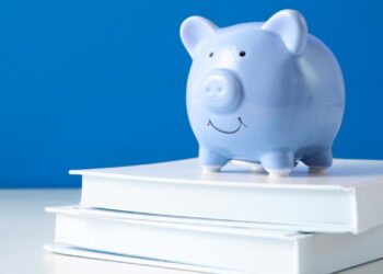 Cofrinho de moedas azul em cima de uma pilha de livros.