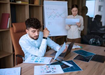 Homem e mulher analisando indicadores da empresa. Ele está sentado e ela em pé.