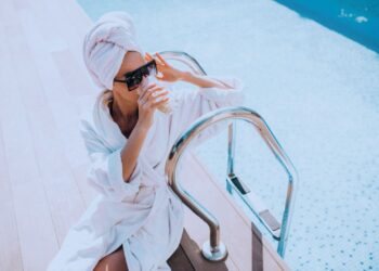 Mulher de roupão tomando um drink à beira da piscina.