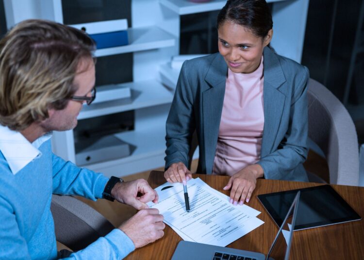 Mulher mostrando algumas informações em um papel para o seu colega de trabalho.