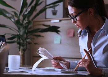 Mulher analisando anotações e fazendo contas na calculadora.