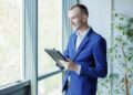 Homem com roupa social segurando um tablet olhando para a janela.