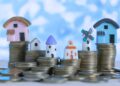 Miniaturas de casas posicionadas em cima de pilhas de moeda.
