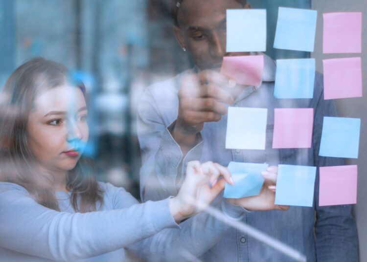 Dois colegas de trabalho colando post-its na parede do escritório.