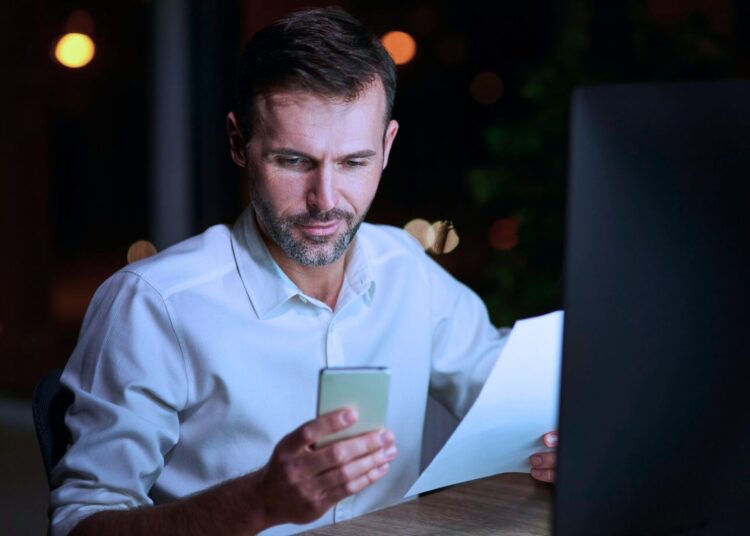 Homem olhando para o celular que está na sua mão.