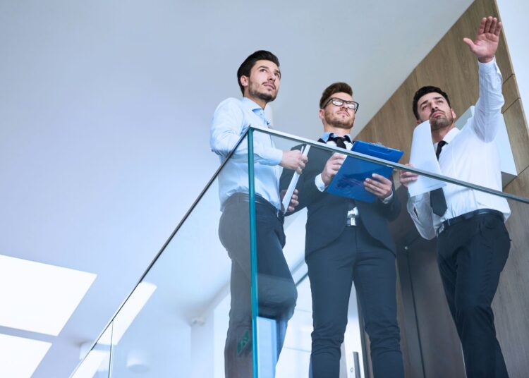 Três homens observando o escritório. Um deles está apontando para algo.