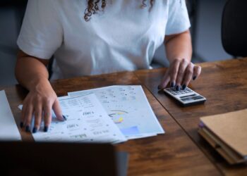 Mulher analisando papéis com dados e gráficos financeiros.