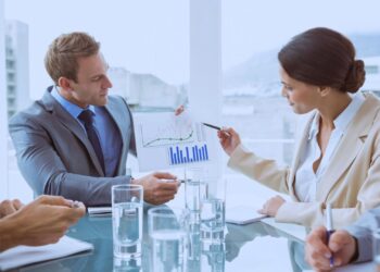 Profissionais discutindo gráficos financeiros em uma reunião corporativa, destacando crescimento e dados de desempenho em um ambiente de escritório moderno e iluminado.