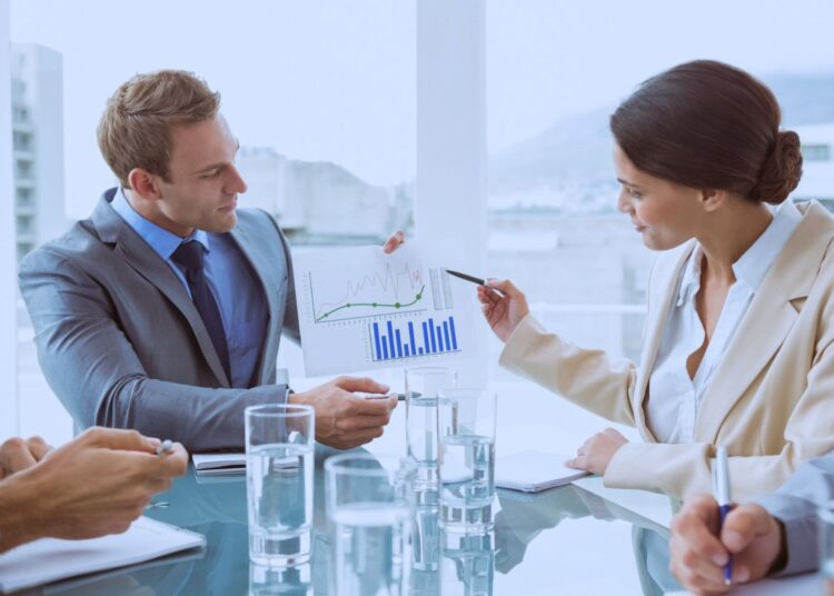 Profissionais discutindo gráficos financeiros em uma reunião corporativa, destacando crescimento e dados de desempenho em um ambiente de escritório moderno e iluminado.