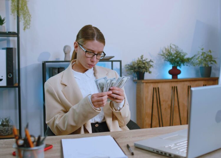 Profissional em um ambiente de escritório analisando cédulas de dinheiro, representando gestão financeira e avaliação de ciclo de caixa.