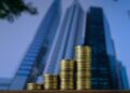 Pilhas crescentes de moedas douradas em primeiro plano, com arranha-céus modernos desfocados ao fundo, simbolizando estrutura de capital, crescimento financeiro e investimentos corporativos.