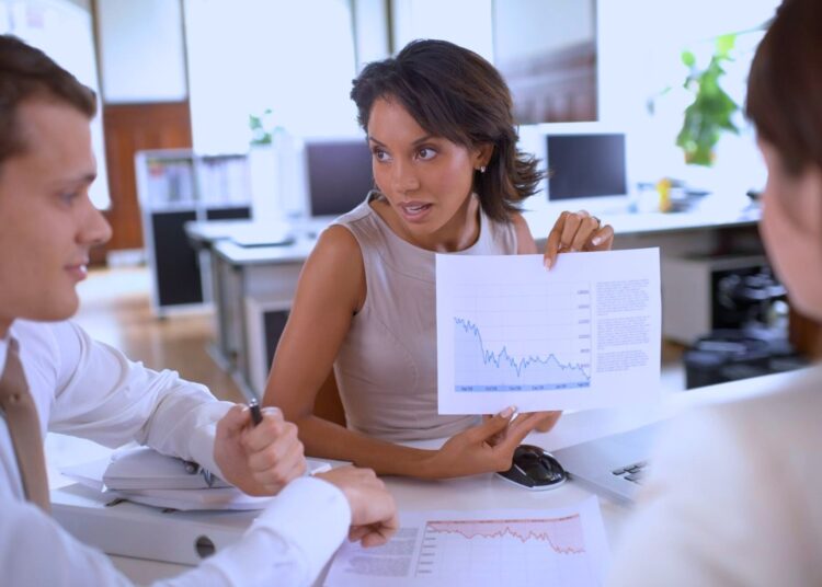 Profissional apresentando gráficos de desempenho financeiro em uma reunião de negócios em um escritório moderno, destacando a análise de índices e tendências de liquidez.