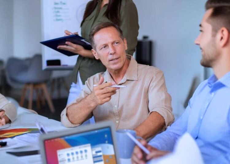 Equipe participando de uma reunião de trabalho com foco em liderança e tomada de decisões, destacando a interação entre os membros e a figura de liderança no centro.
