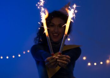 Mulher segurando sparkles acesos em um ambiente festivo e iluminado, simbolizando celebração e entusiasmo com foco em metas e resoluções para o Ano Novo.
