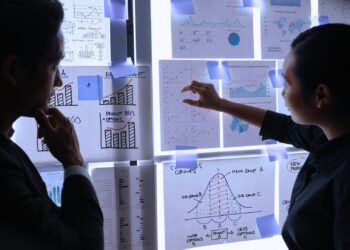 Dois profissionais analisando gráficos e dados em um painel iluminado, representando planejamento operacional e estratégias baseadas em informações detalhadas.