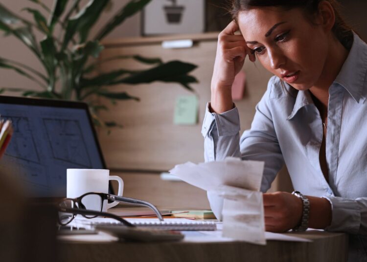 Mulher analisando documentos financeiros em um escritório, representando o conceito de despesas antecipadas.