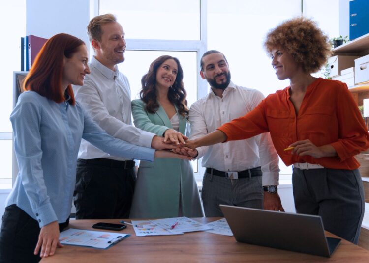 Equipe de vendas unida celebrando o sucesso com mãos juntas em gesto de motivação e colaboração, destacando o trabalho em equipe e a energia positiva no ambiente corporativo.