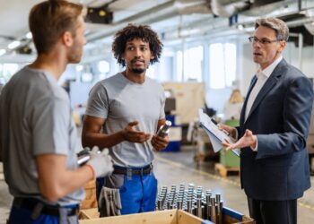 Gestor discutindo com equipe de colaboradores em fábrica sobre processos de gestão de fornecedores e produção industrial.