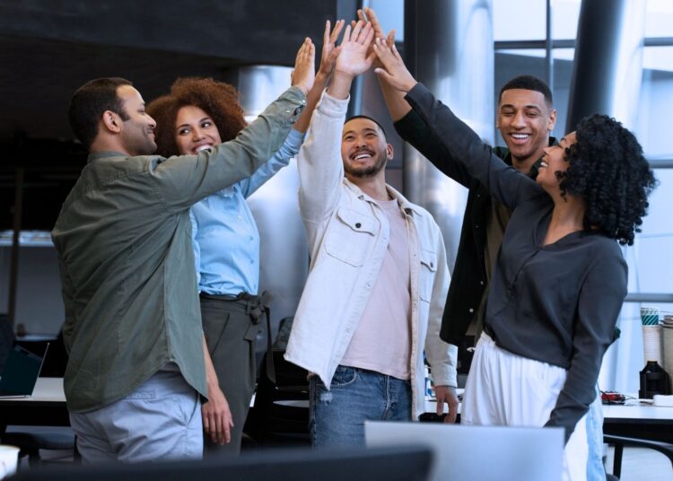 Equipe de trabalho comemorando sucesso com um high five coletivo, simbolizando união, motivação e reconhecimento no ambiente corporativo.