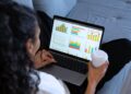 Mulher analisando gráficos financeiros em um laptop enquanto segura um copo de café, representando planejamento financeiro e gestão de investimentos para 2025.