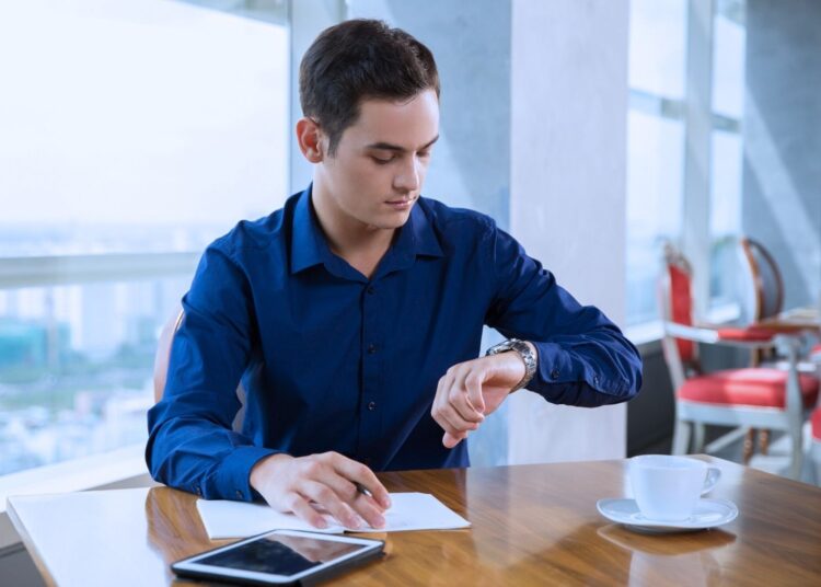 Imagem de um homem verificando o relógio enquanto trabalha, representando a gestão do prazo médio de pagamento no contexto empresarial.