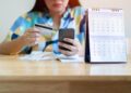 Mulher analisando faturas e usando cartão de crédito para pagamento, com calendário ao lado, representando o uso do cheque especial.