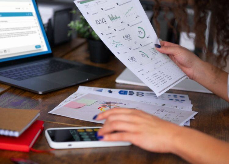 Mulher analisando documentos financeiros e gráficos, representando a importância da DRE e do DFC na gestão empresarial.