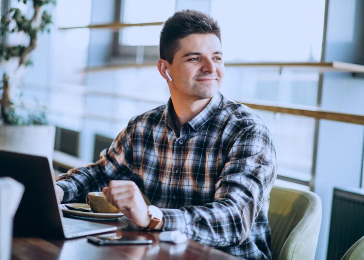 Profissional jovem da geração Y, sentado em um ambiente moderno, trabalhando com laptop e fones de ouvido, representando conectividade e produtividade no mercado de trabalho atual.