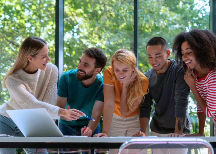 Jovens da geração Z trabalhando em equipe, discutindo ideias em frente a um laptop, representando inovação e finanças no mercado atual.