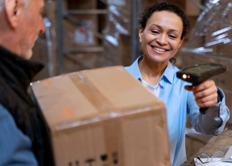 Funcionária sorridente escaneando código de barras em uma caixa em um armazém, representando o controle do giro de estoque.