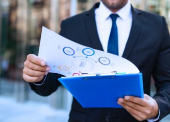 Empresário segurando prancheta com gráficos e dados empresariais, representando análise comparativa entre lucro presumido e lucro real.