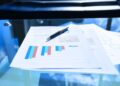 Documentos financeiros com gráficos de barras coloridos sobre uma mesa de vidro, representando a estrutura financeira de uma empresa.