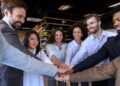 Equipe diversa unindo as mãos em sinal de colaboração e engajamento, representando a liderança servidora no ambiente corporativo.
