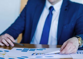 Executivo de terno azul analisando gráficos financeiros em documentos sobre regime de caixa e controle contábil.