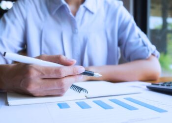 Mão segurando uma caneta sobre relatório financeiro com gráficos, simbolizando a antecipação do imposto de renda e planejamento tributário.