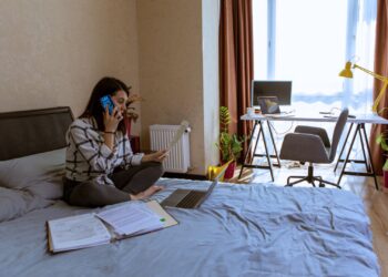 Mulher trabalhando em home office, analisando documentos e falando ao telefone, representando o prazo para declarar o imposto de renda.