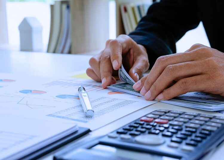 Pessoa contando dinheiro ao lado de uma calculadora e gráficos financeiros, representando planejamento financeiro e controle de crédito rotativo.