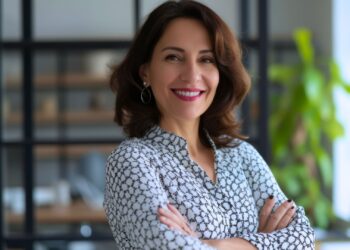 Mulher sorridente de braços cruzados em ambiente corporativo moderno, transmitindo confiança e profissionalismo, representando liderança no planejamento financeiro empresarial.