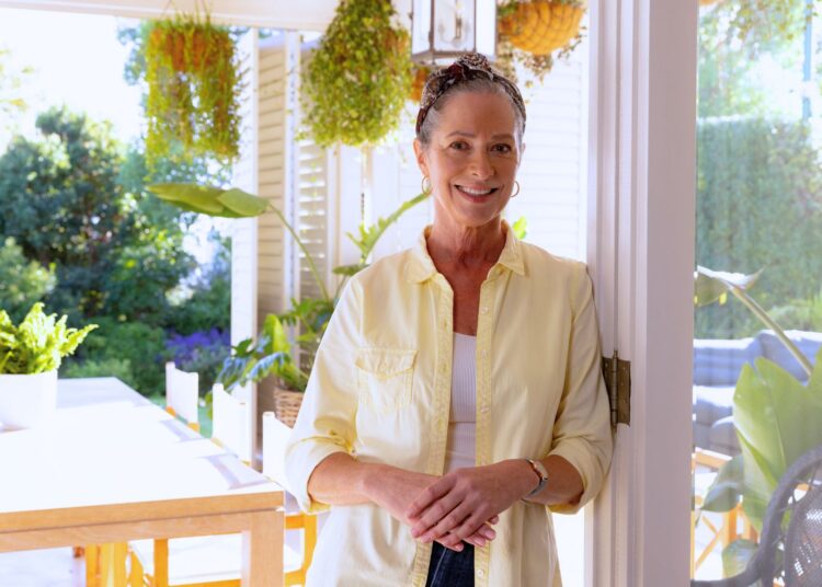 Mulher sorridente em varanda residencial bem iluminada, representando proprietária de imóvel que busca empréstimo com terreno de garantia para viabilizar projetos pessoais ou profissionais com melhores condições de crédito.