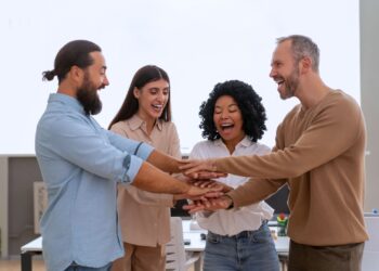 cultura na empresa: quatro colegas em um escritório juntando as mãos em sinal de união e engajamento de equipe.